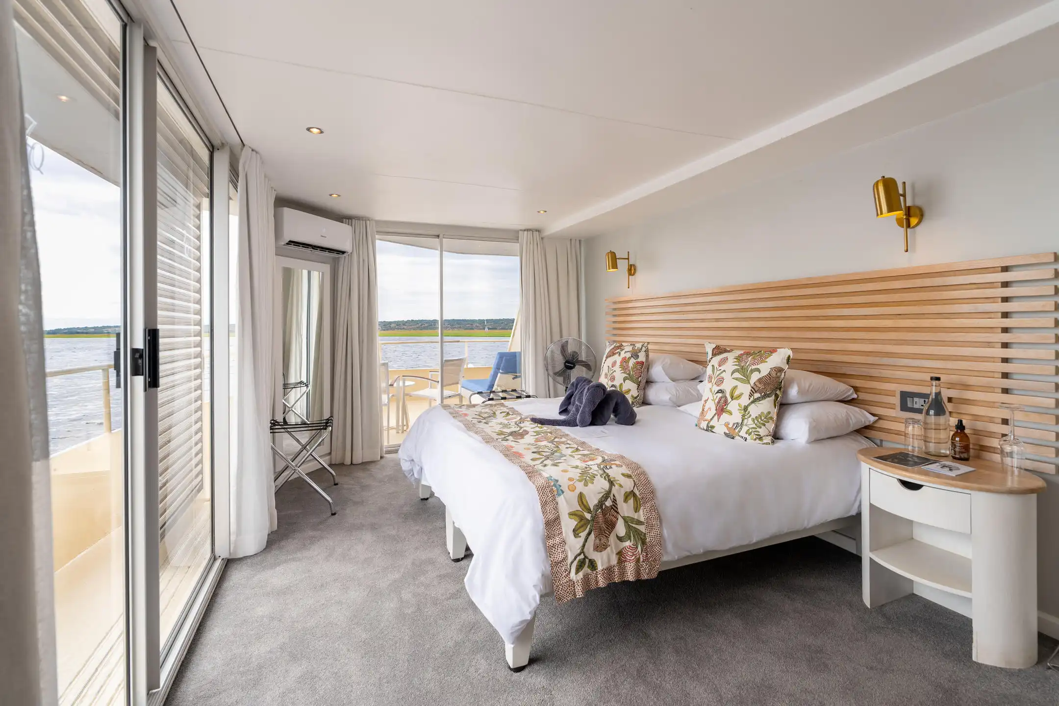 Luxury cabin on an African photo safari river cruise, featuring a plush bed and balcony with river views.