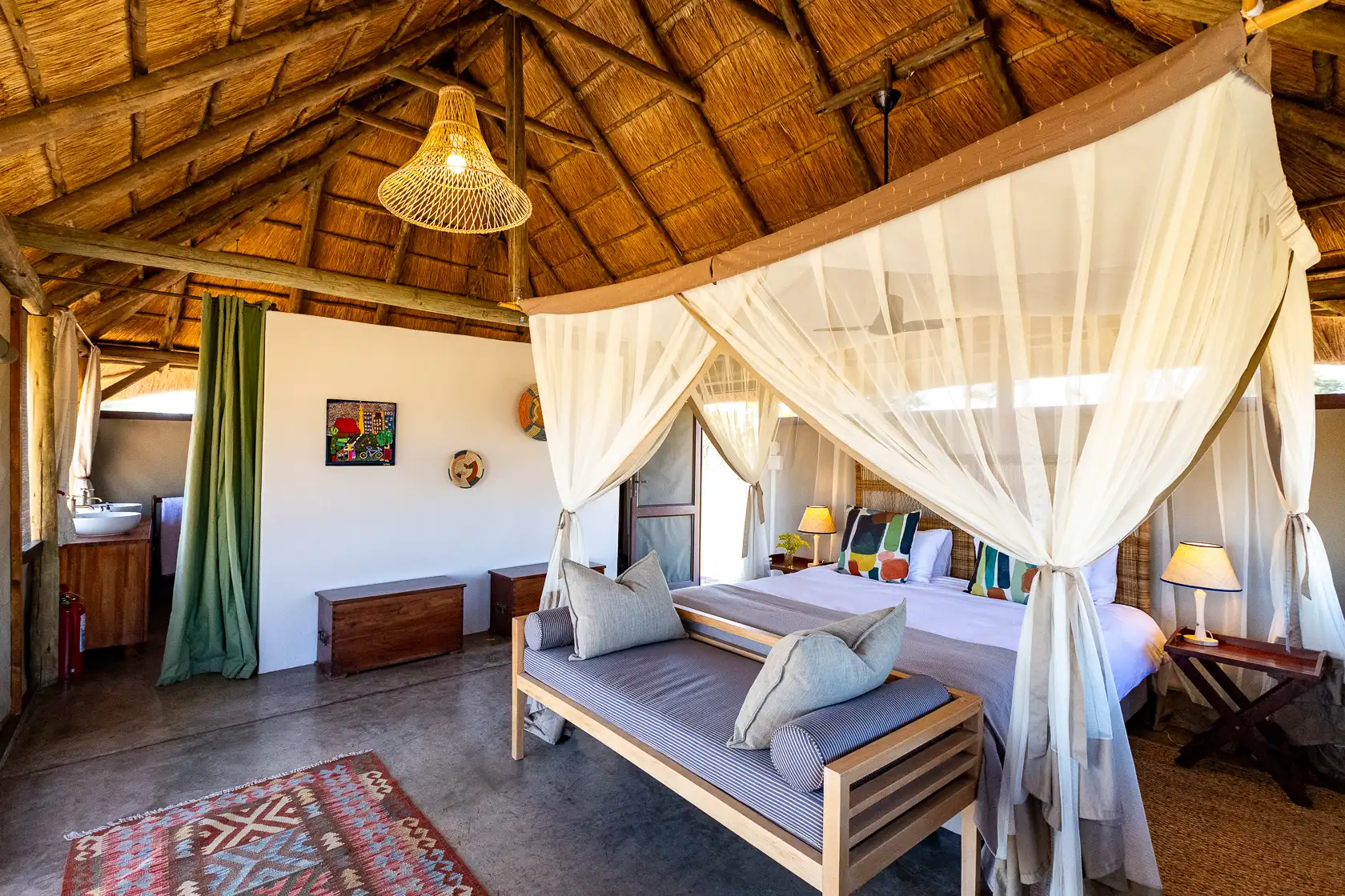 Camp Hwange safari lodge bedroom with four-poster bed, thatched roof, and African decor. Photo safari.