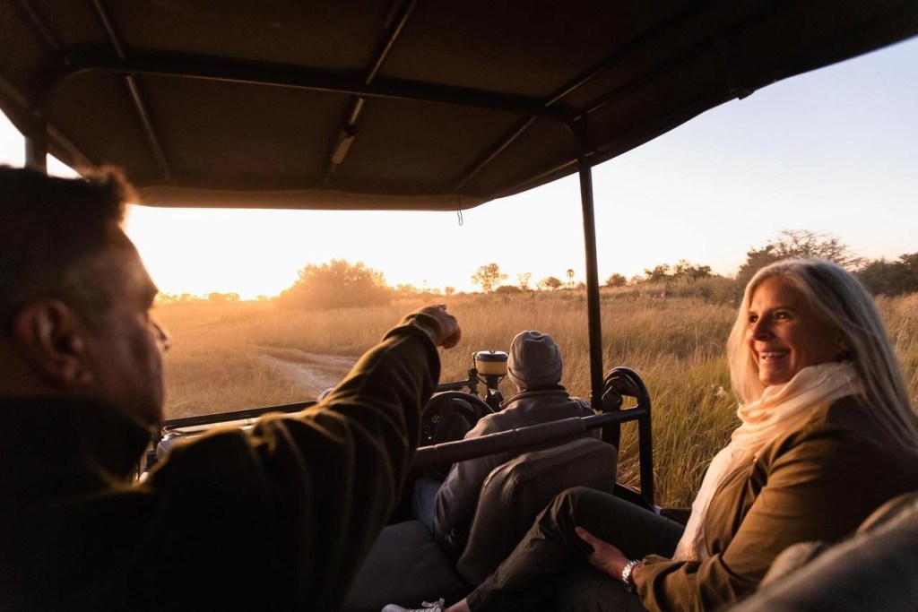 African photo safari: Tourists in open vehicle at sunset, enjoying wildlife viewing.