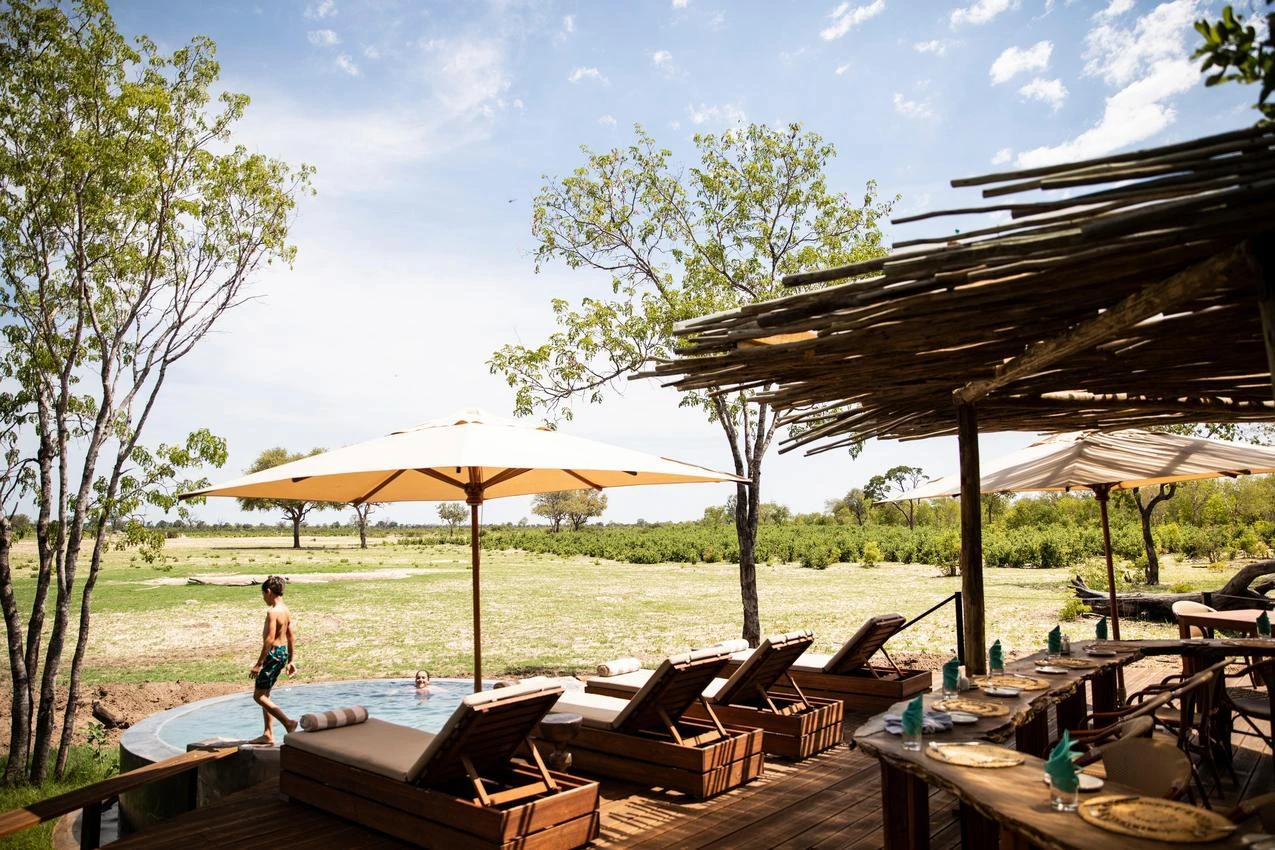 Luxury African safari lodge with pool, lounge chairs, and dining area overlooking the savanna.