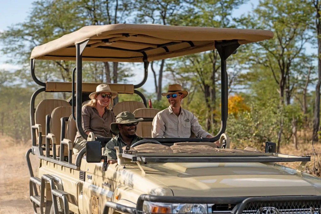 African photo safari: Tourists in open-top safari vehicle with guide, enjoying a wildlife tour.