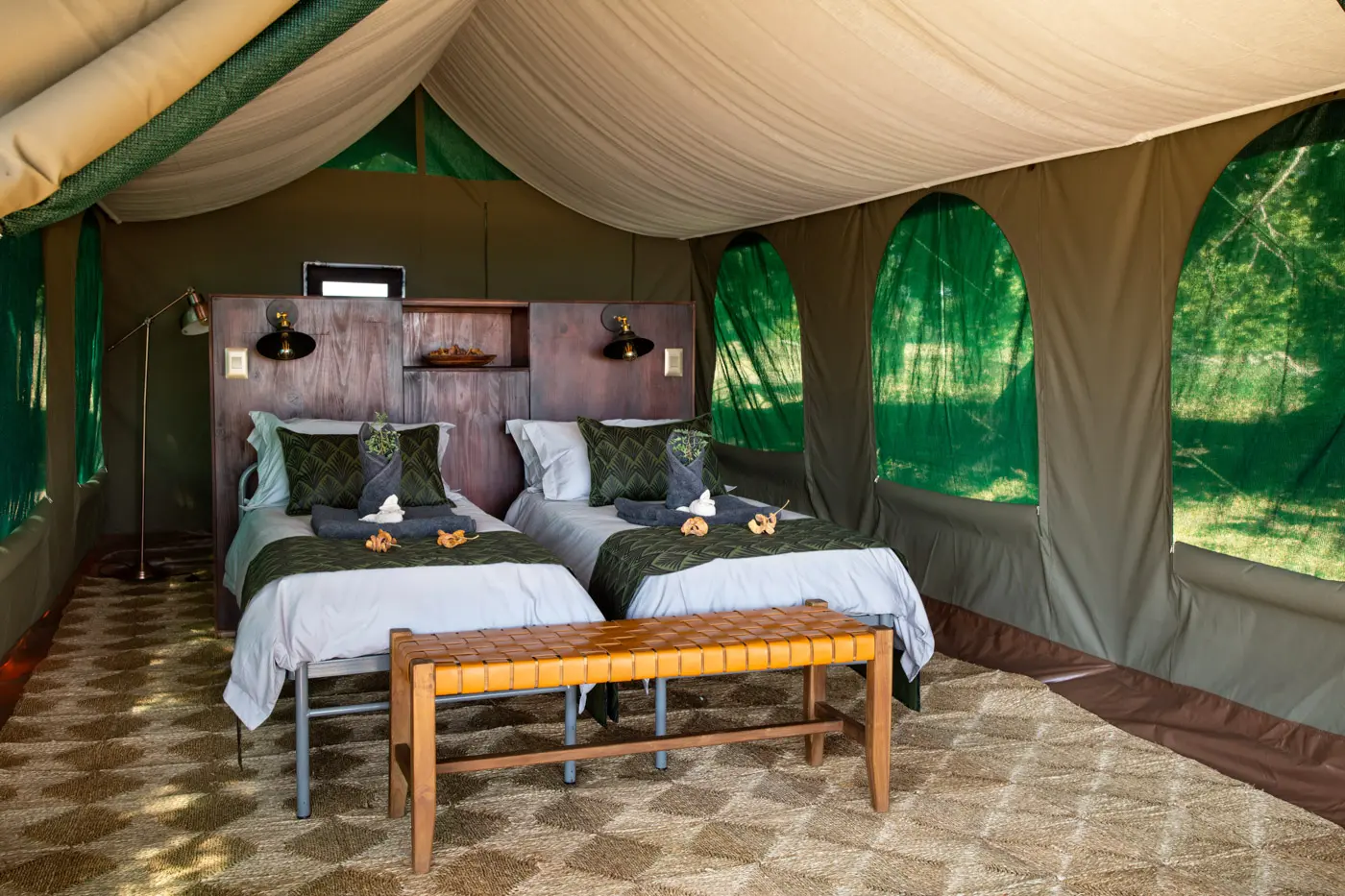Two twin beds in a safari tent with a wooden bench and large windows