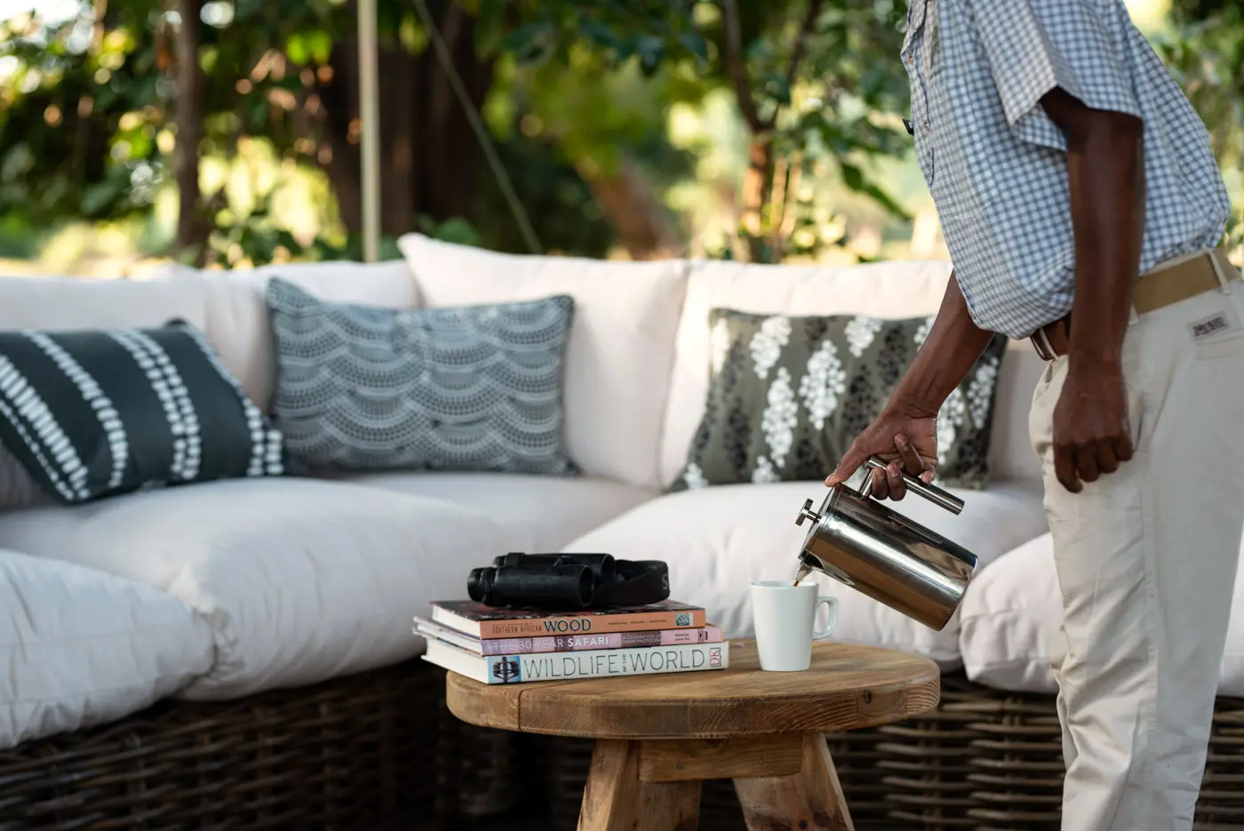 African photo safari: Person pours coffee near binoculars and wildlife books on a rustic table.