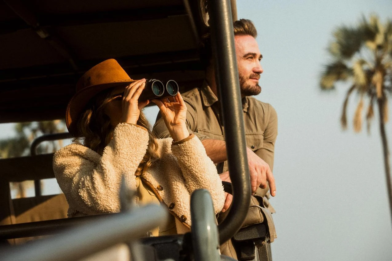 Couple on African photo safari, woman using binoculars. Adventure travel.