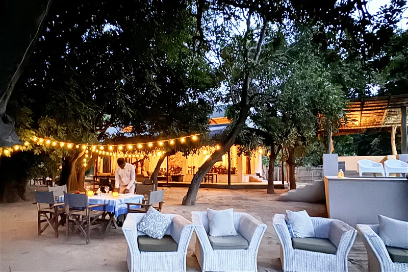 South Luangwa safari lodge at dusk: outdoor dining, string lights, wicker seating. Photo safari experience.
