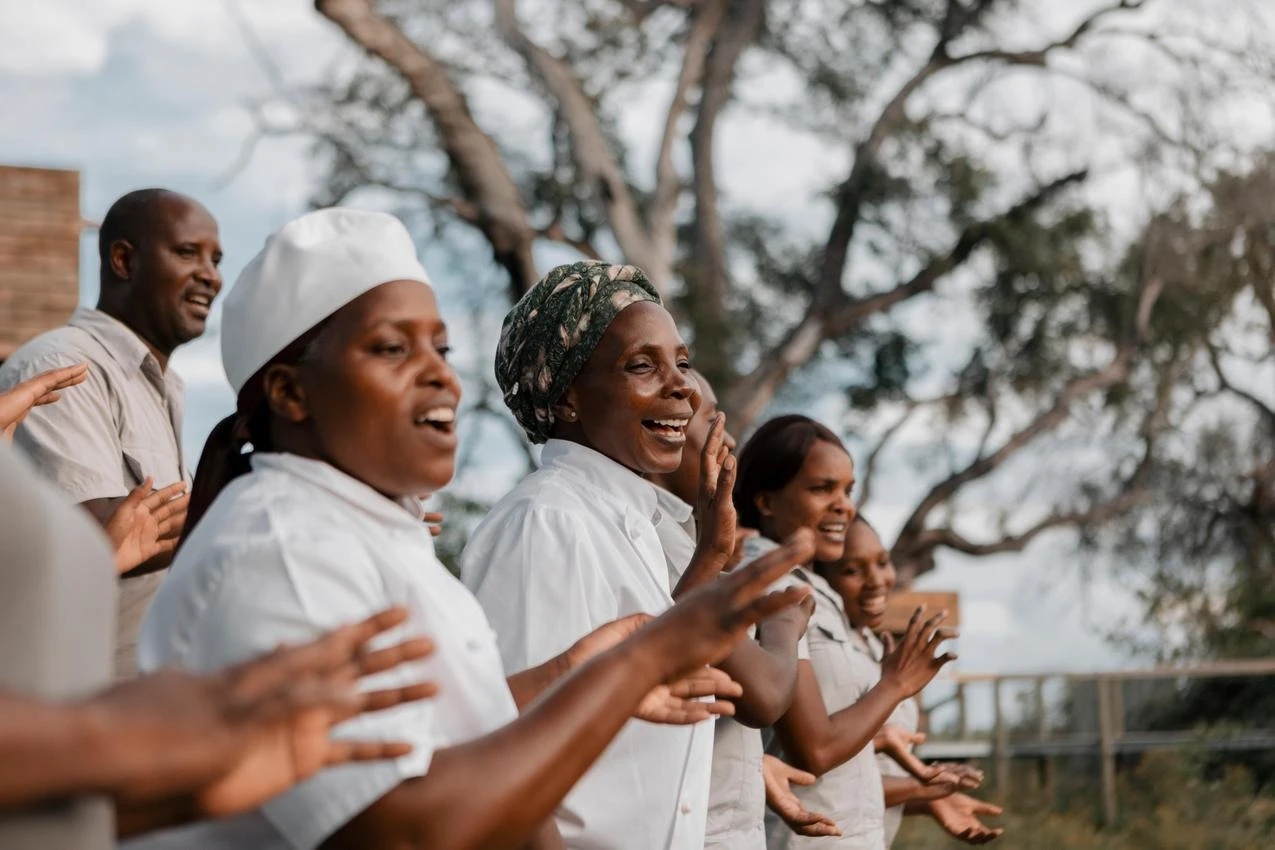 Group of smiling African workers cheering outside, possibly on a photo safari in Africa.