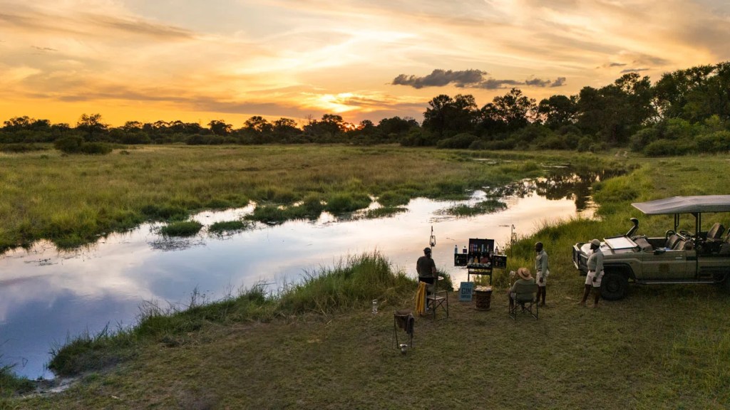 African photo safari at sunset: People gather by a river with a safari vehicle, enjoying the scenic landscape.