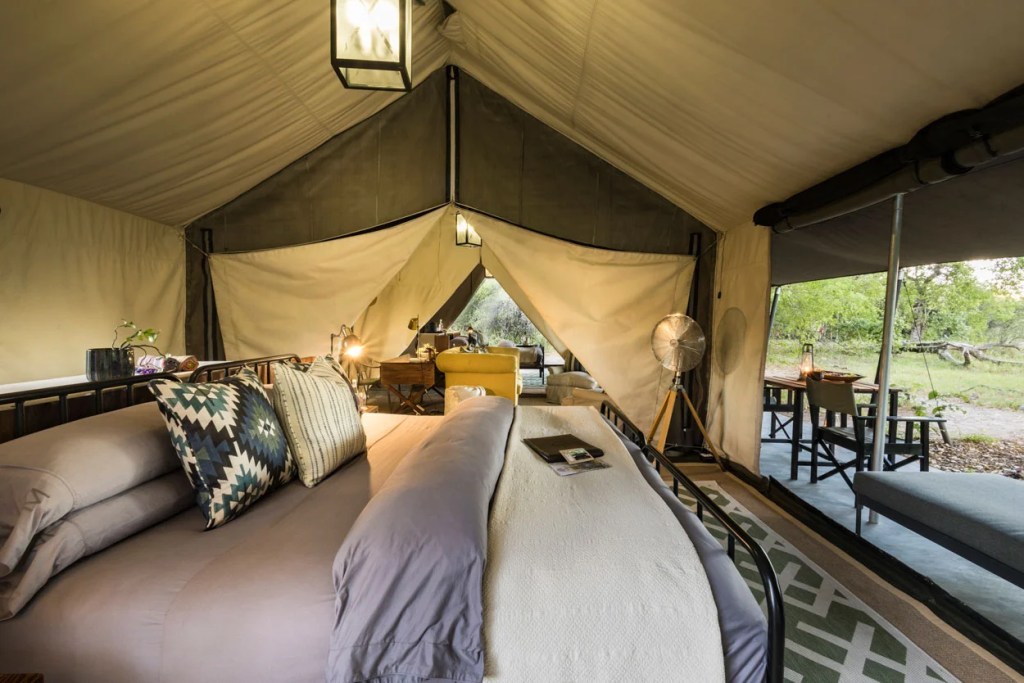 Luxury safari tent interior with bed, desk, and outdoor dining area. African safari ambiance. Photo safari experience.