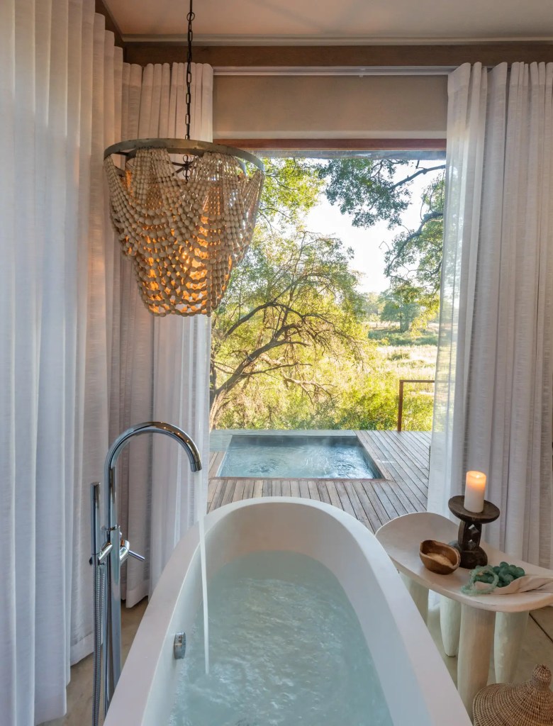 Bathtub in open-air bathroom with view of small pool and tree