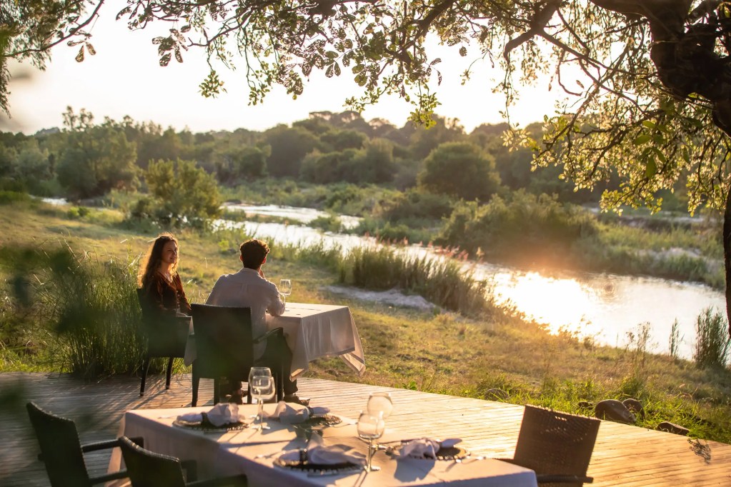 Couple dining outdoors on African safari during Uganda expedition, scenic river view.
