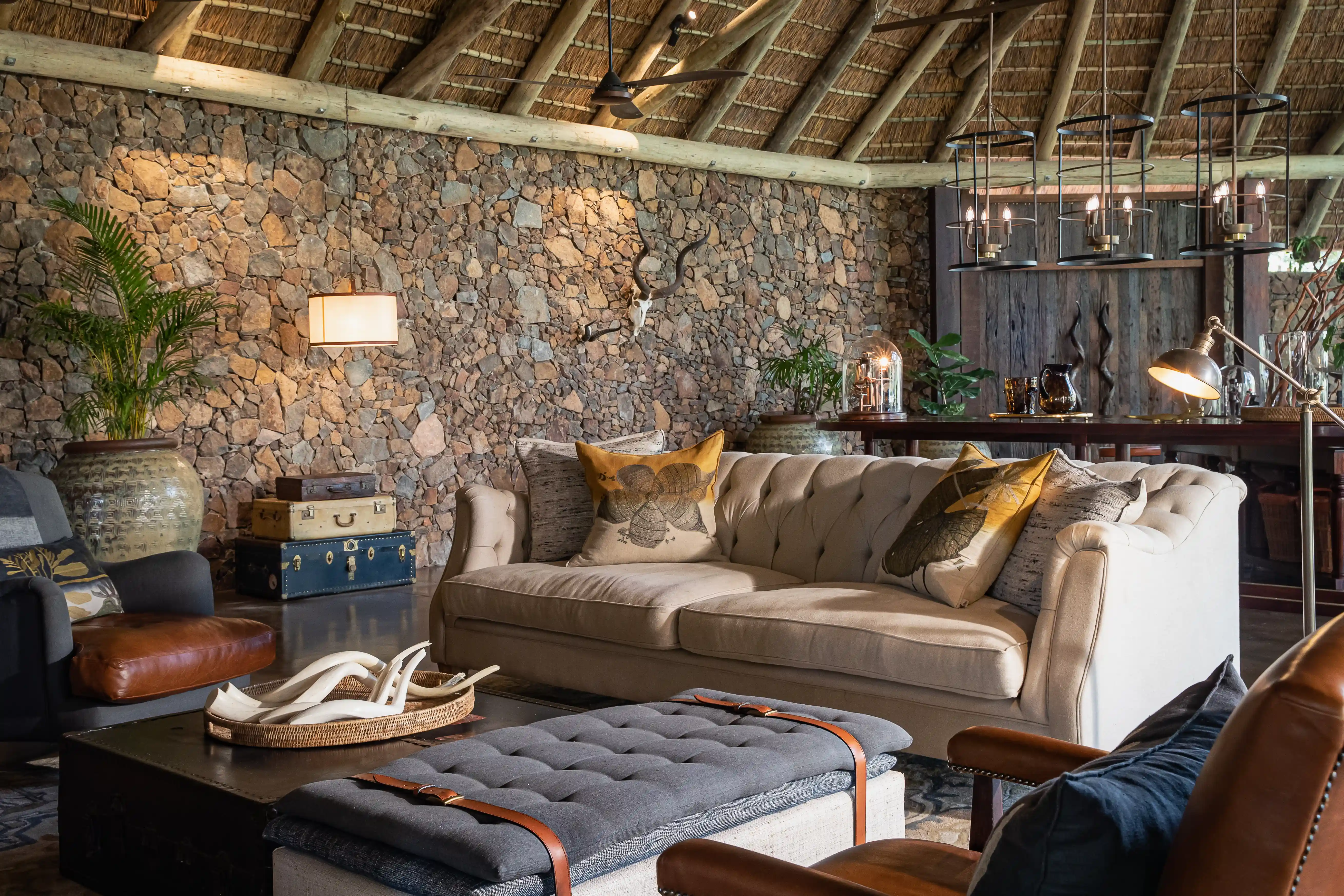Luxury African safari lodge living room with stone walls, thatched roof, and comfortable seating.
