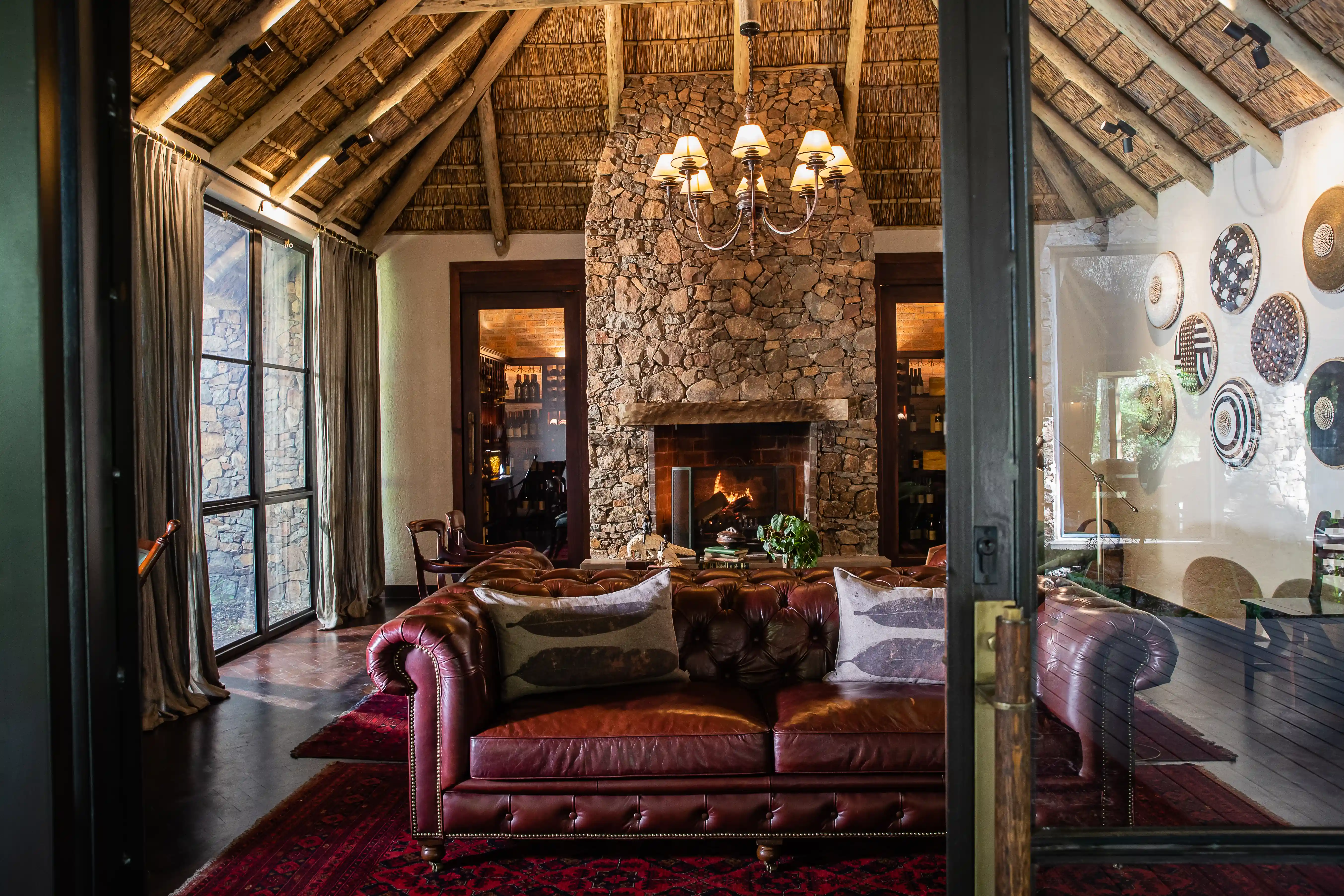 Luxury Sabi Sand lodge interior: leather sofa, stone fireplace, thatched roof, African safari decor.