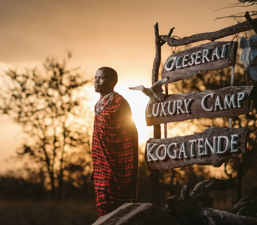 Maasai warrior in Serengeti at sunset, with sign for Oleserai Luxury Camp, photo safari.