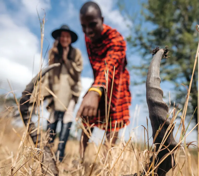 Masai guide and tourist on Serengeti photo safari, pointing at animal tracks.