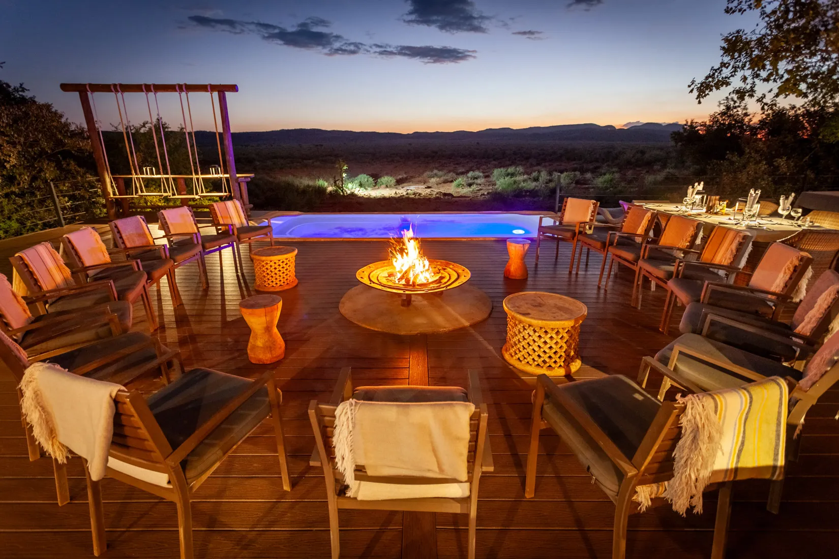 African safari lodge deck with fire pit, pool, and chairs at dusk