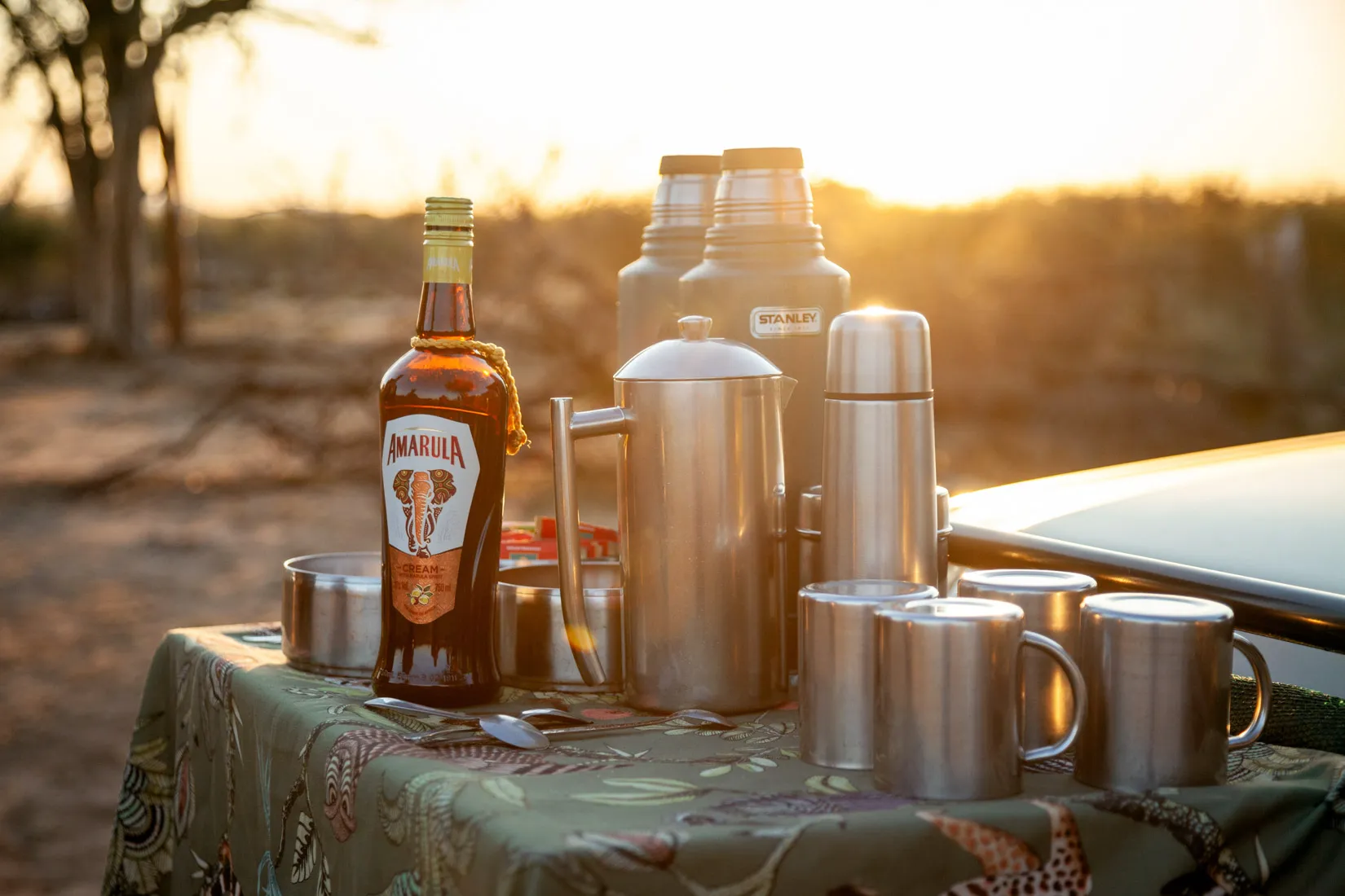 African safari morning: Amarula bottle, thermoses, mugs on a table during a photo safari.
