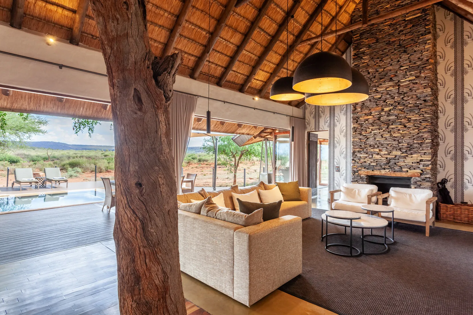 Luxury safari lodge living room with thatch roof and stone fireplace, Madikwe