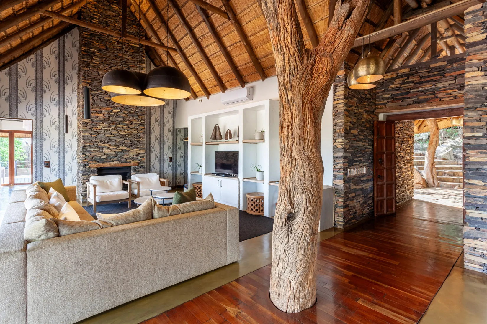 Luxury safari lodge living room with thatched roof, stone walls, and tree trunk